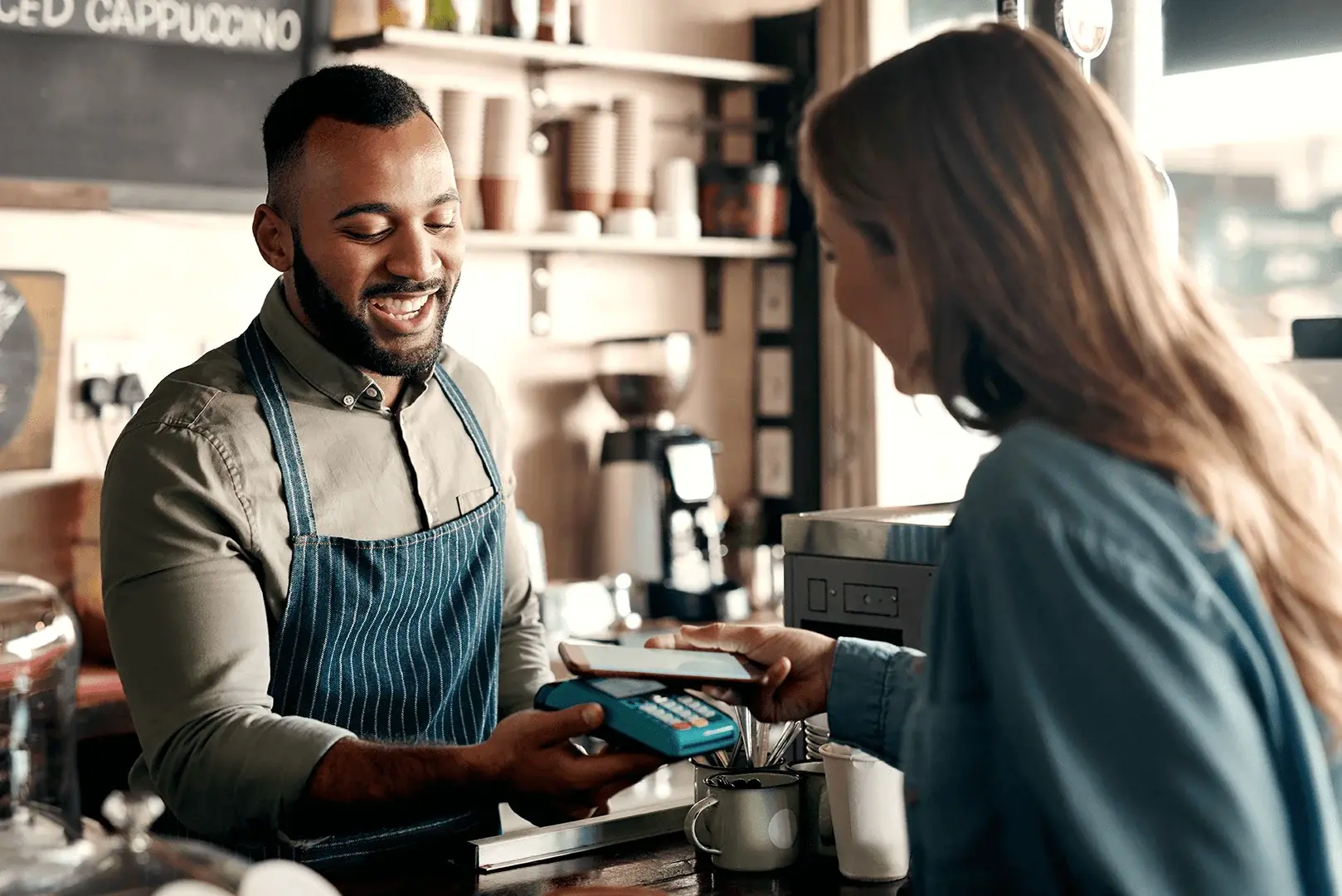 Eine Frau bezahlt einen Mann in einem Café und gibt ihm Trinkgeld über ein Kartenlesegerät. 