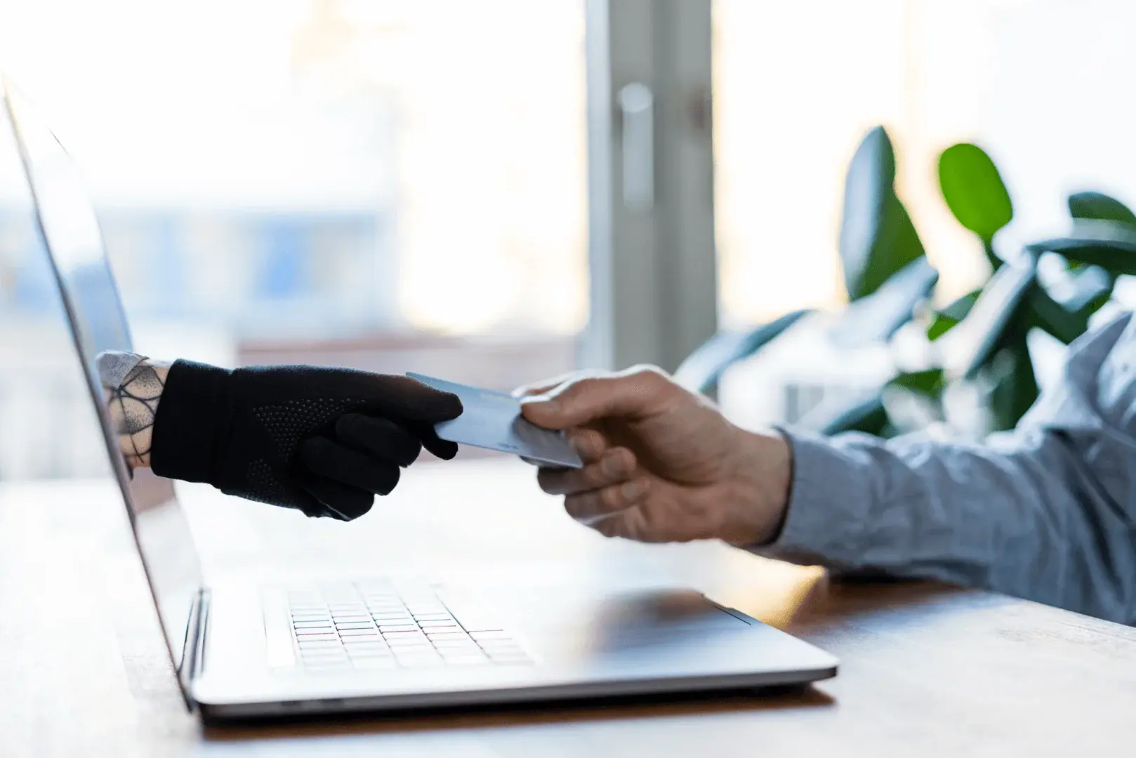 Foto: Eine Hand, mit schwarzem Handschuh, die aus dem Laptop kommt, schnappt sich die EC-Karte, die ein Mann in Richtung Laptop hält.