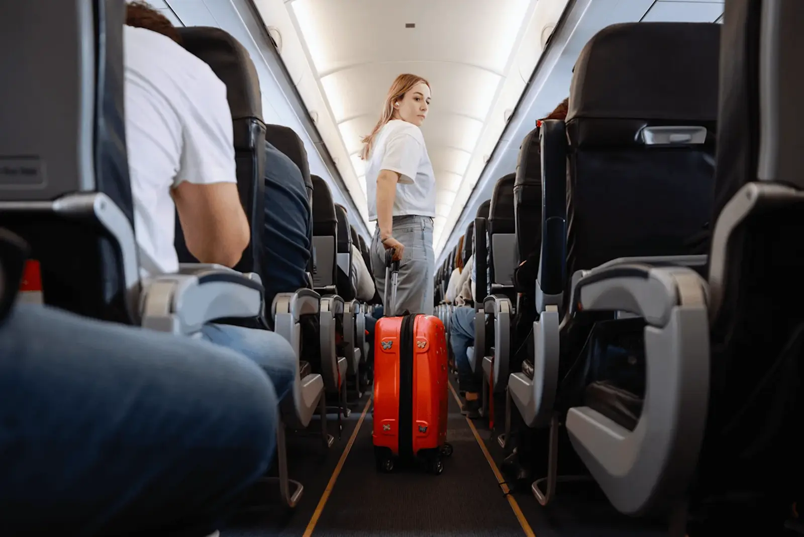 Foto: eine junge Frau zieht ihr Handgepäck durch den Gang im Flugzeug.