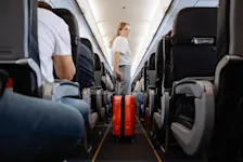 Foto: eine junge Frau zieht ihr Handgepäck durch den Gang im Flugzeug.
