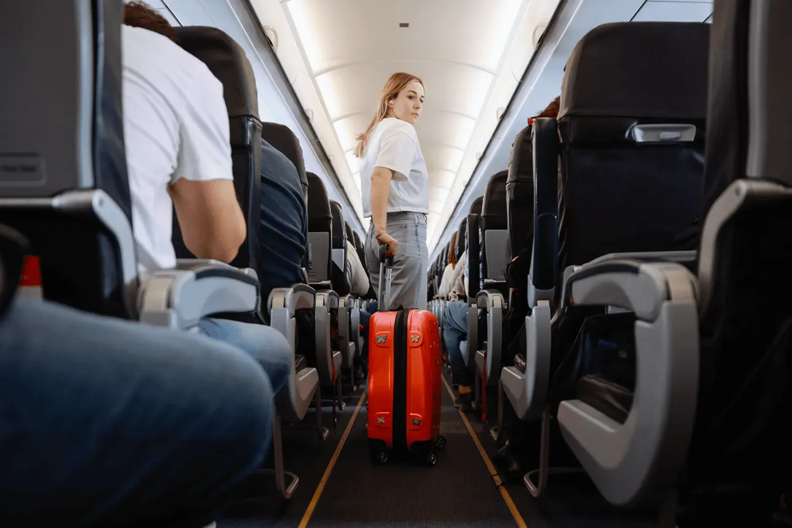Foto: eine junge Frau zieht ihr Handgepäck durch den Gang im Flugzeug.