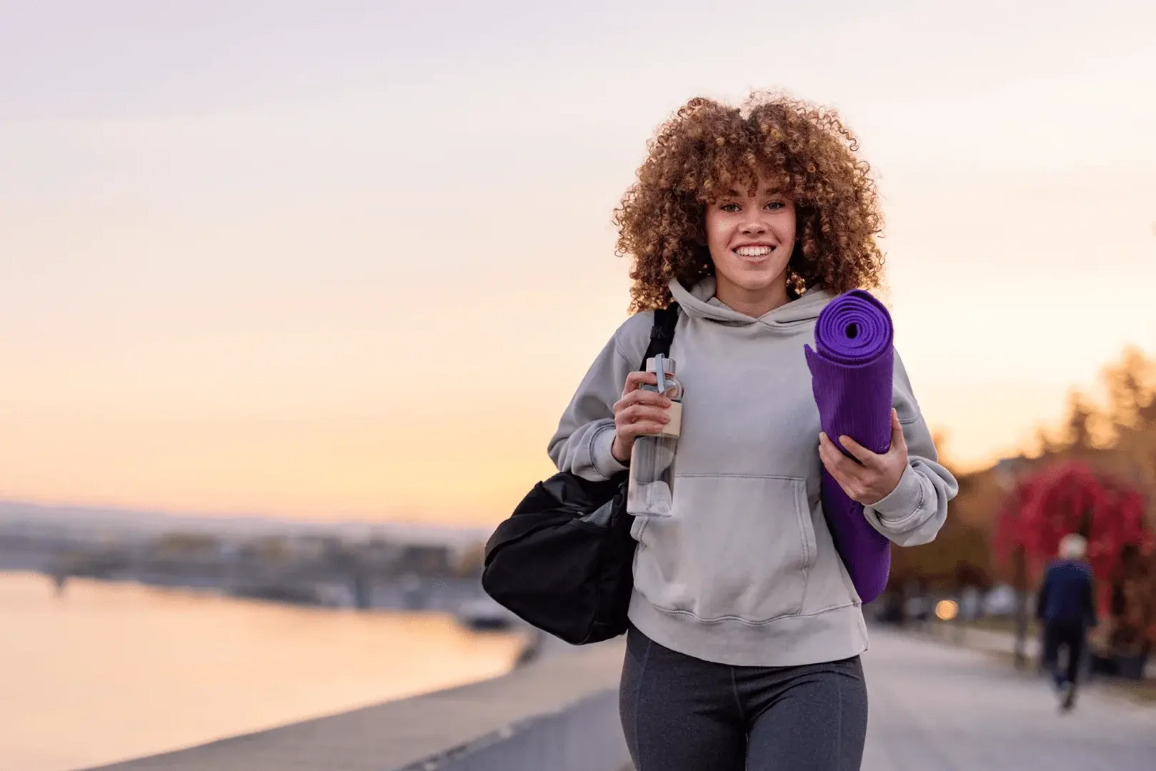 Foto: eine junge Frau geht mit Yoga-Matte und Sporttasche zum Fitnessstudio