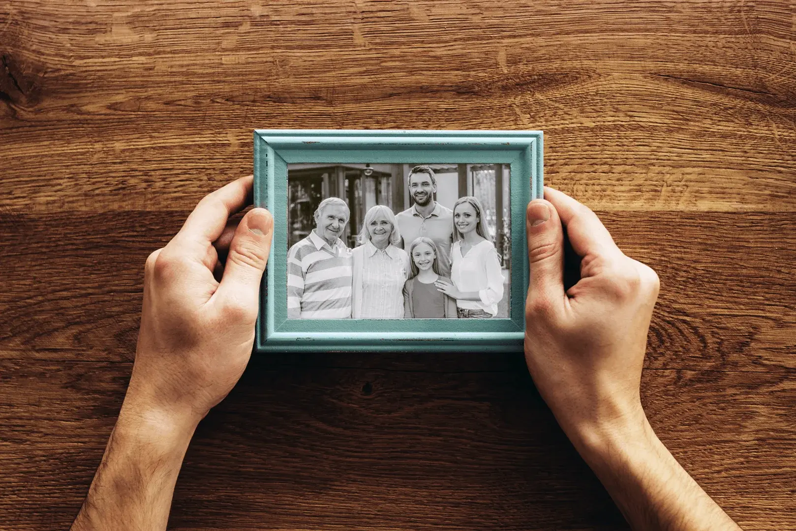 Foto: eine Person hält ein gerahmtes Foto. Auf dem Foto sieht man eine Familie.