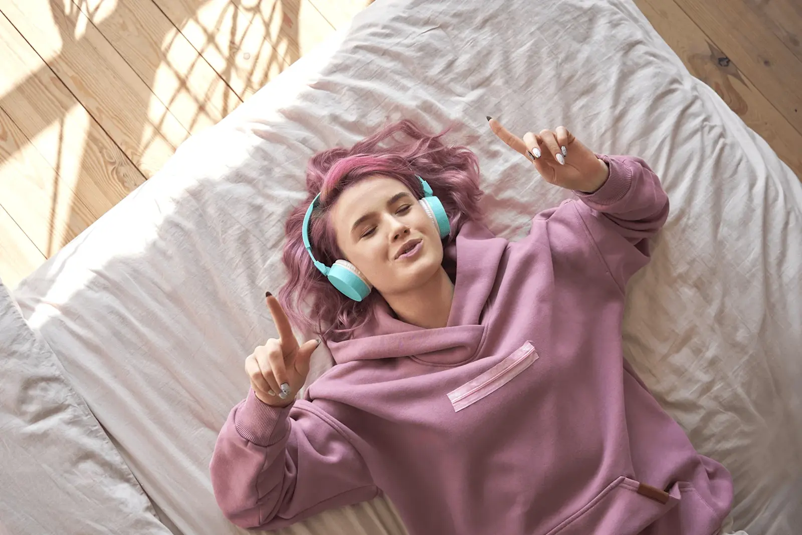 Foto: ein Teenie mit pinken Haaren liegt auf dem Bett und hört Spotify