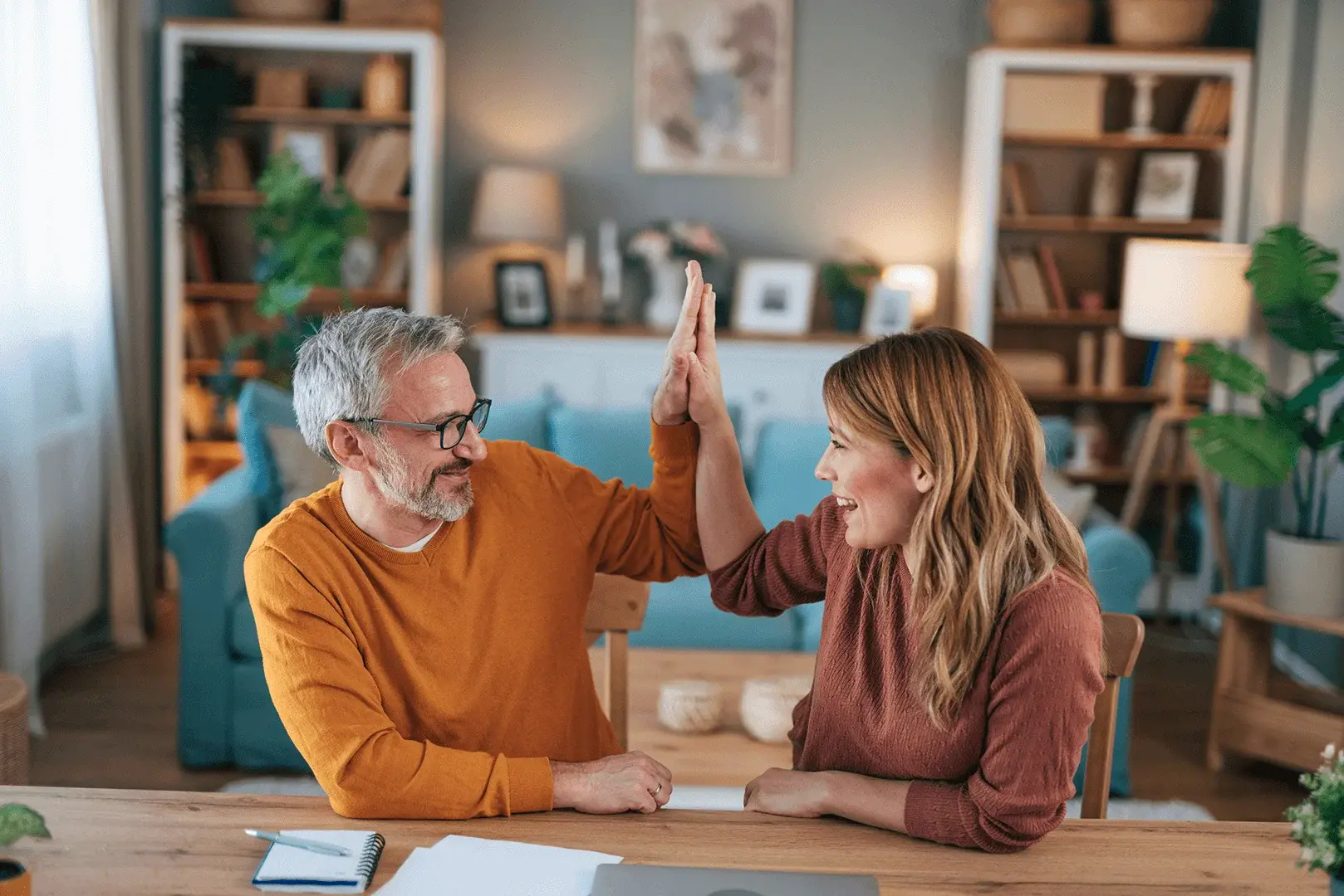 Ein Mann und eine Frau feiern an einem Tisch mit einem High Five, beide strahlen Freude aus