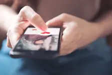 Foto: eine Person hält ein Smartphone in der Hand und hat eine Dating-App geöffnet.