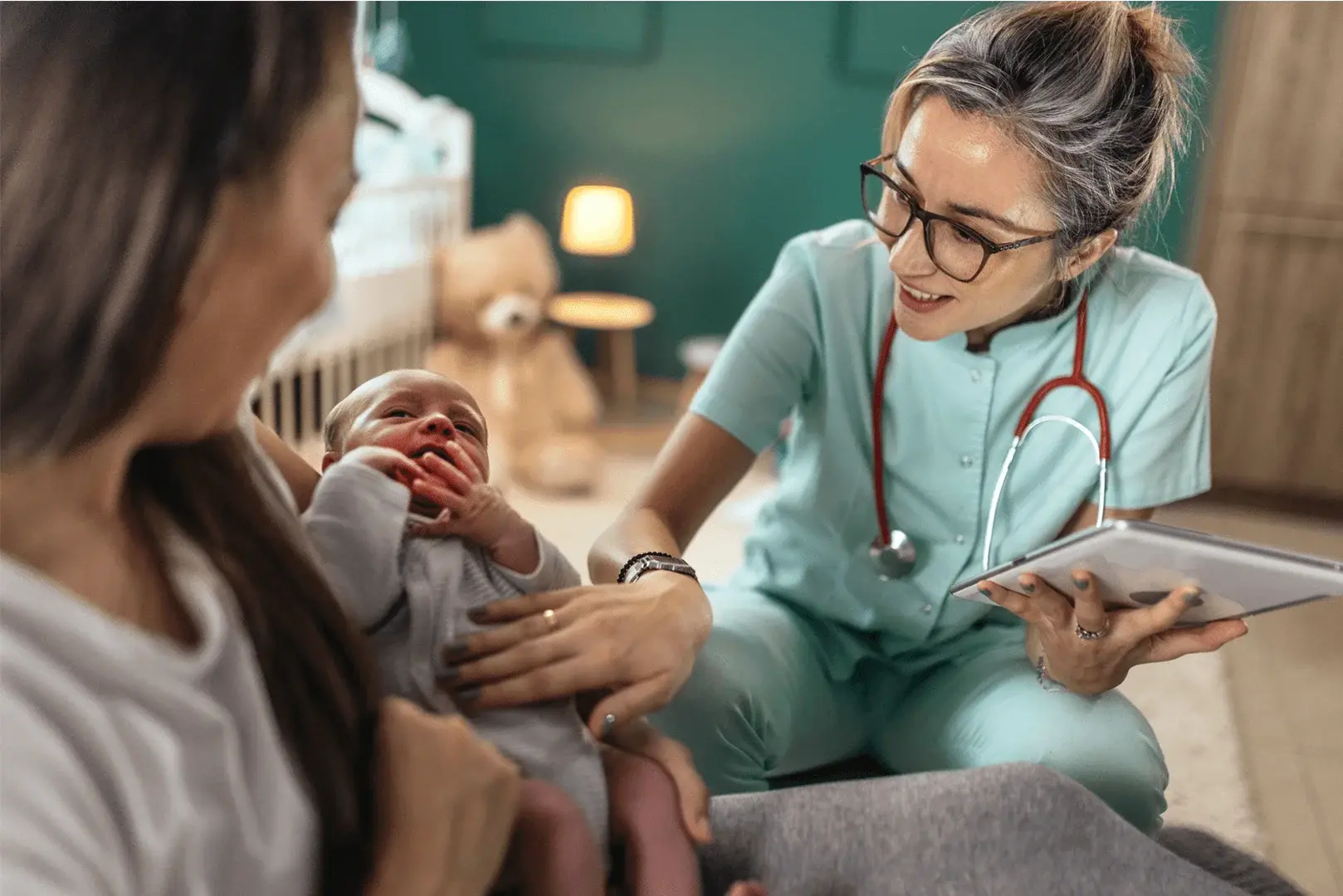 Foto: eine Mutter hält ihr Neugeborenes und eine Hebamme schaut nach dem Rechten.