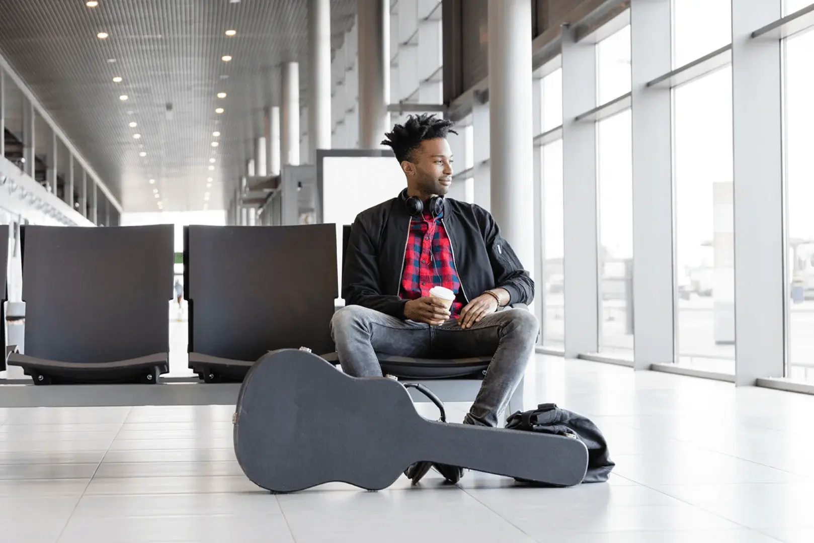 Foto: Musiker sitzt am Flughafen. Vor sich steht sein Gitarrenkoffer