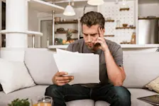 Mann liest besorgt ein Dokument auf der Couch.