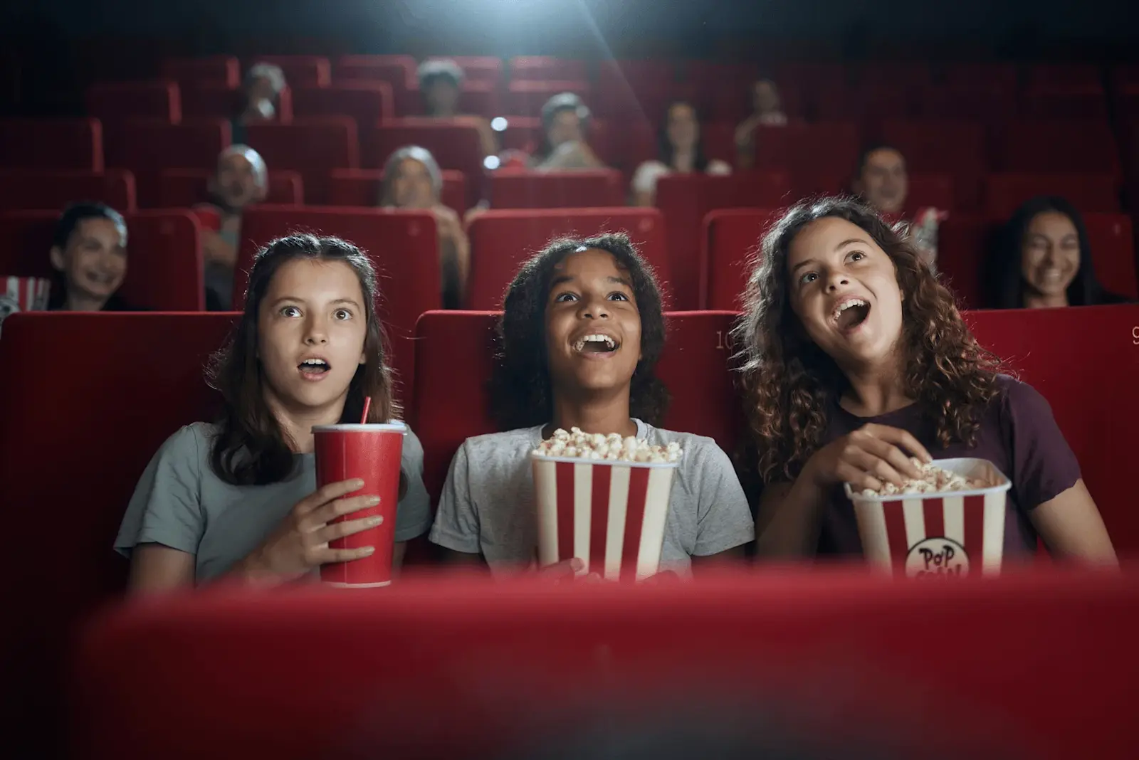 Foto: drei Kinder sitzen im Kino mit Popcorn und sind begeistert