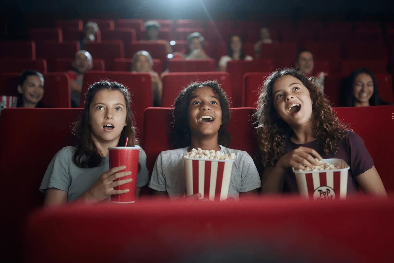 Foto: drei Kinder sitzen im Kino mit Popcorn und sind begeistert
