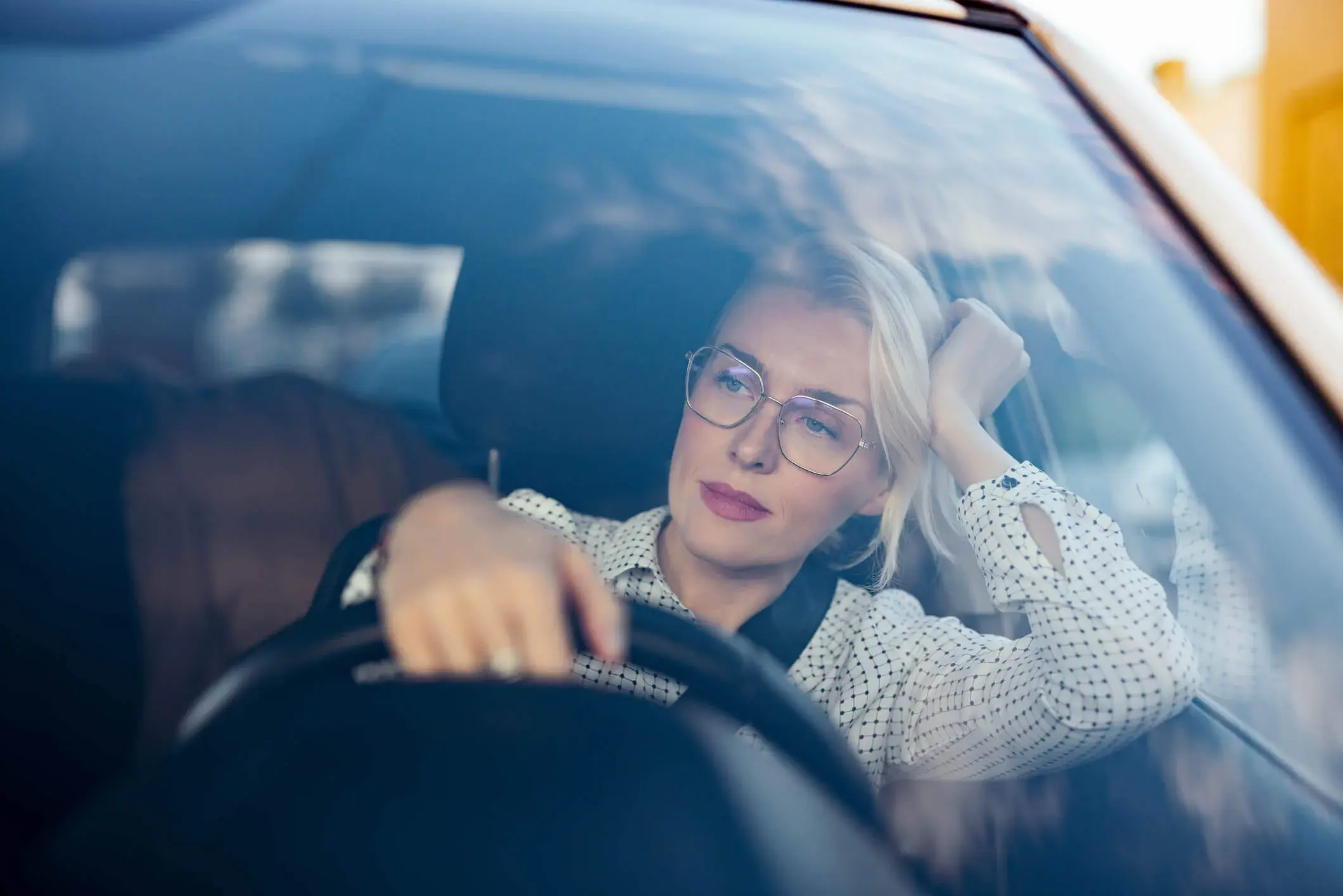 Eine Frau mit Brille sitzt am Steuer eines Autos und blickt nachdenklich auf die Straße.