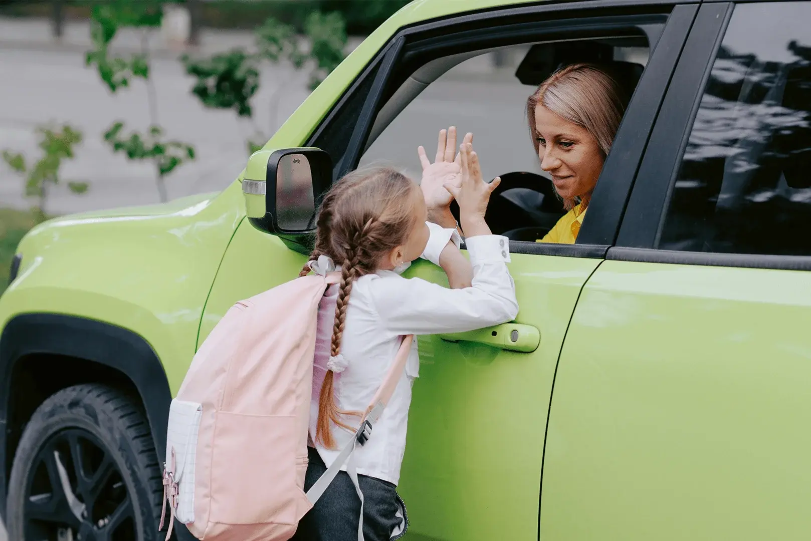 Foto: ein Mädchen, mit Schultasche, verabschiedet sich von ihrer Mutter, die noch im Auto sitzt.
