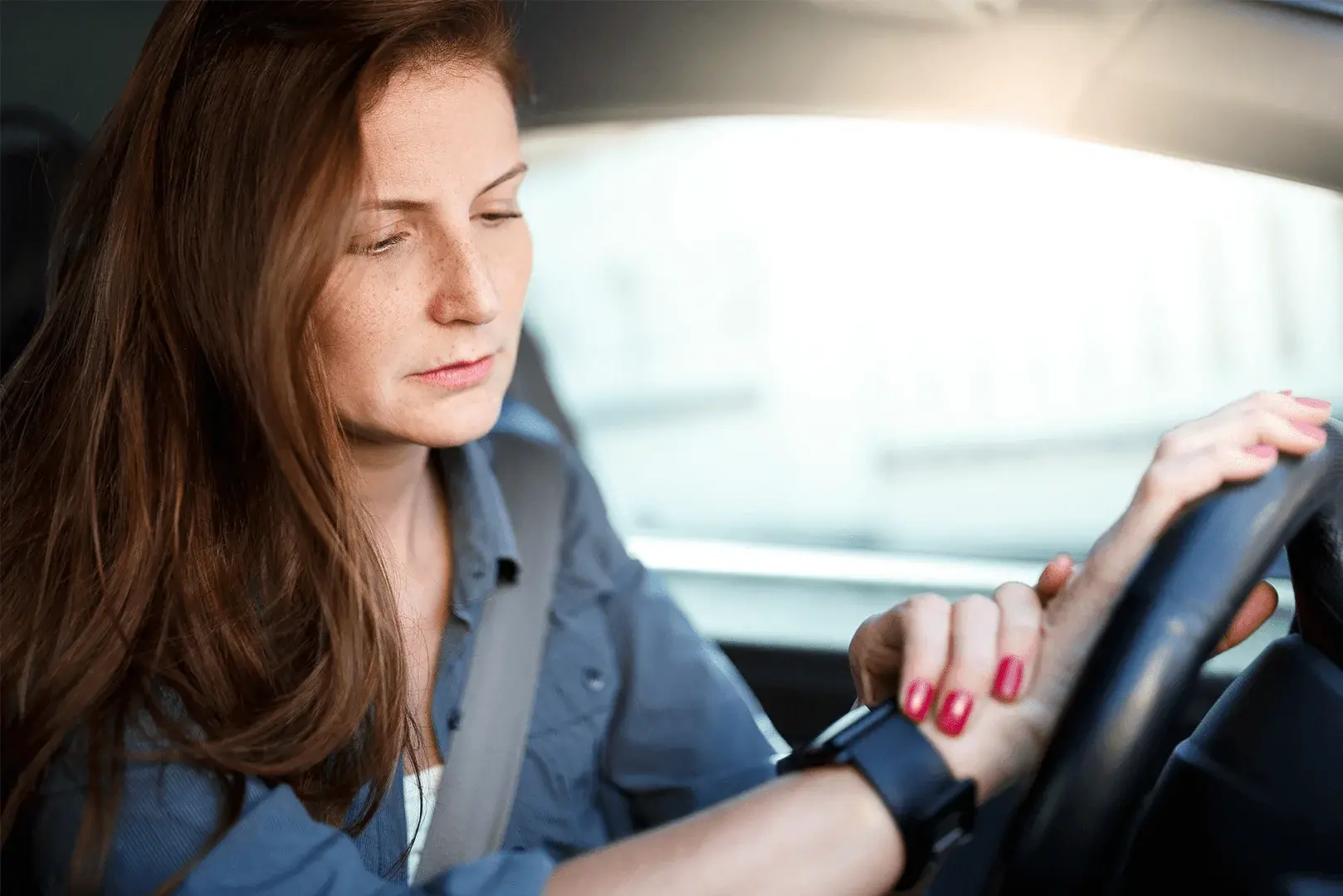 Eine Frau sitzt am Steuer ihres Autos und schaut auf ihre Smartwatch.