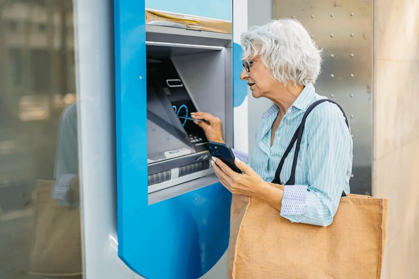 Foto: eine ältere Frau mit Brille steht an einem Automaten und schaut angestrengt auf das Display.