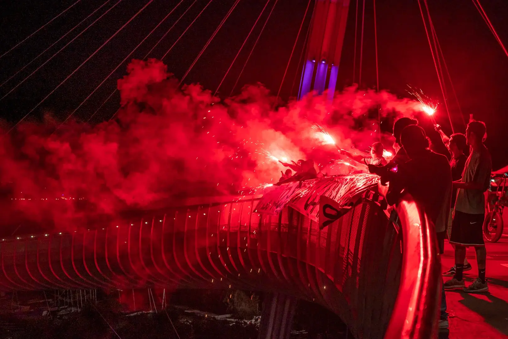 Fußball-Fans auf einer Brücke, umhüllt von rotem Rauch, zeigen ihre Begeisterung und feiern mit Pyrotechnik.