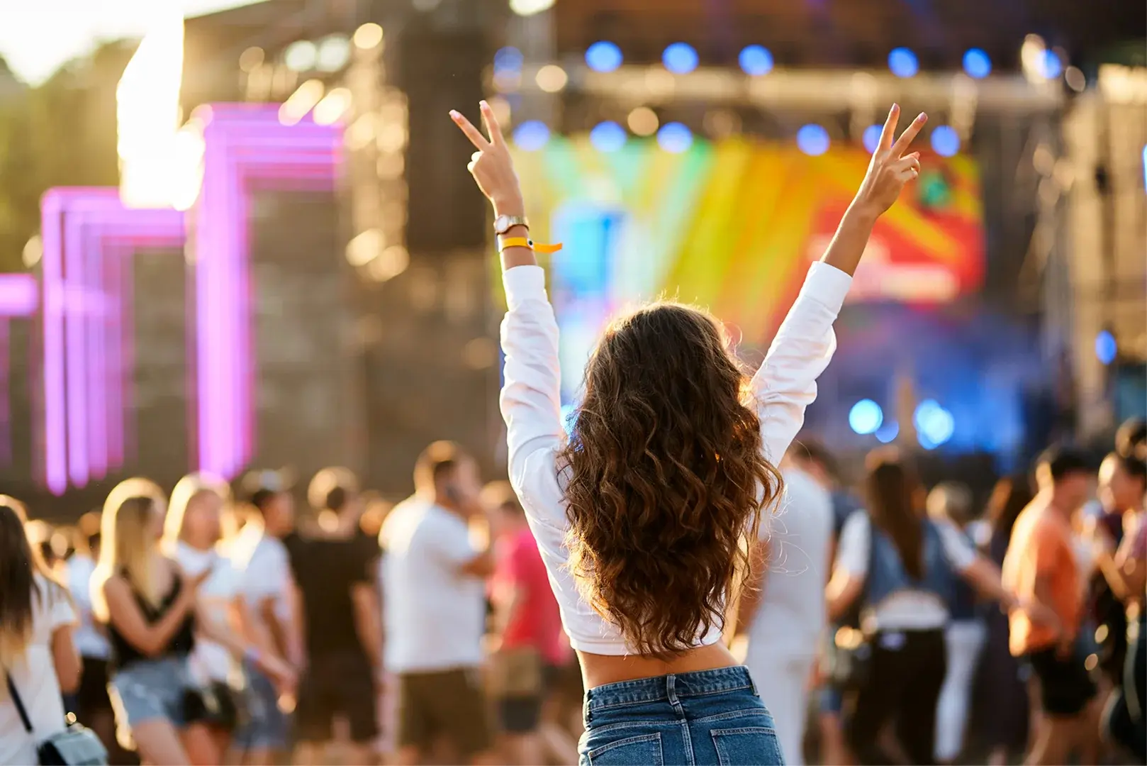Das Foto zeigt eine Frau die ihre Arme in die Luft streckt vor einer Festivalbühne.