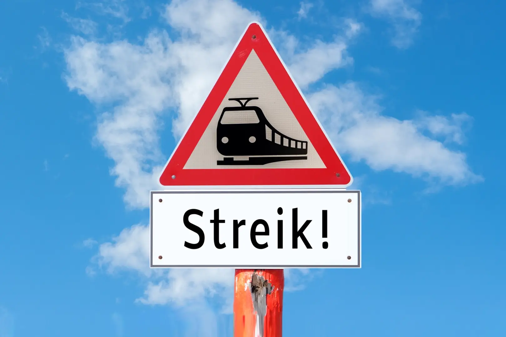 Ein Schild mit der Aufschrift "Strik" im Vordergrund, während ein Zug im Hintergrund zu sehen ist.