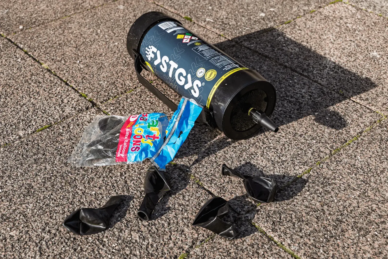 Foto: eine Lachgas Flasche mit Luftballons liegen auf der Straße