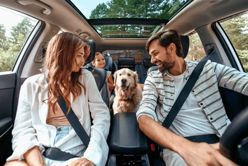 Eine fröhliche Familie sitzt mit ihrem Hund im Auto, bereit für eine sichere Reise.