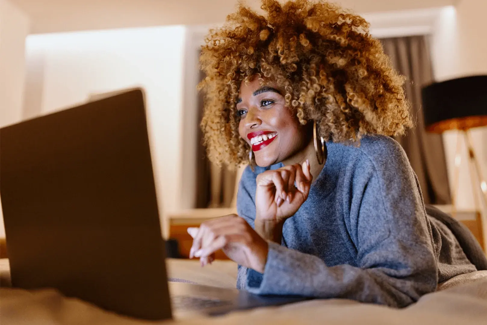 Eine Frau mit lockigem Haar liegt auf ihrem Bett und nutzt ihren Laptop für Online-Shopping.