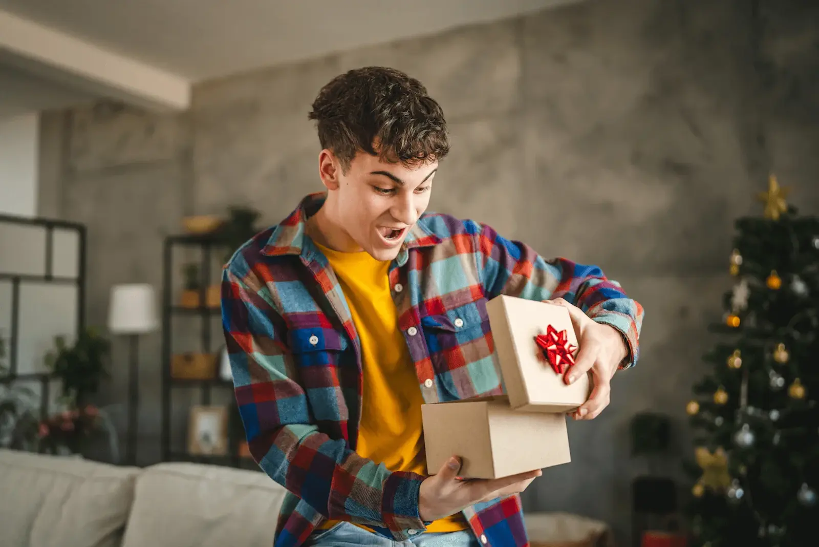 Foto: ein Jugendlicher öffnet sein Geschenk mit voller Überraschung zu Weihnachten.