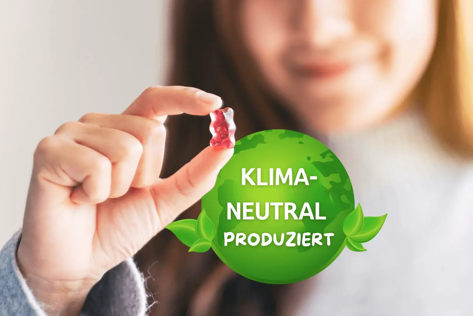 Foto: eine Frau hält ein Weingummi in ihrer Hand, daneben ein Logo zur Klimaneitralität.