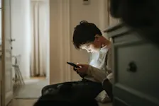 Foto: Ein Schulkind sitzt im Flur und starrt in sein Handy.