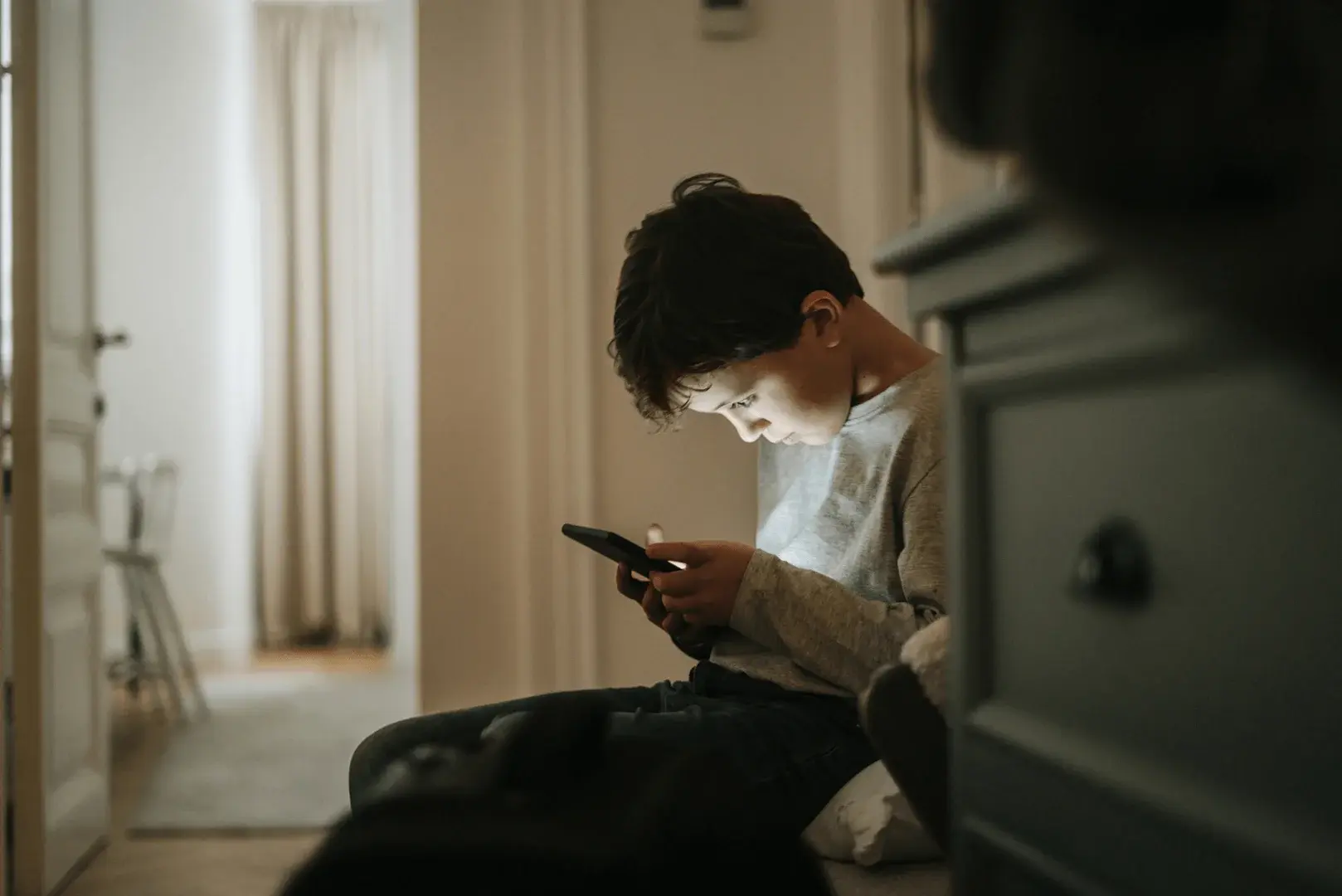 Foto: Ein Schulkind sitzt im Flur und starrt in sein Handy.