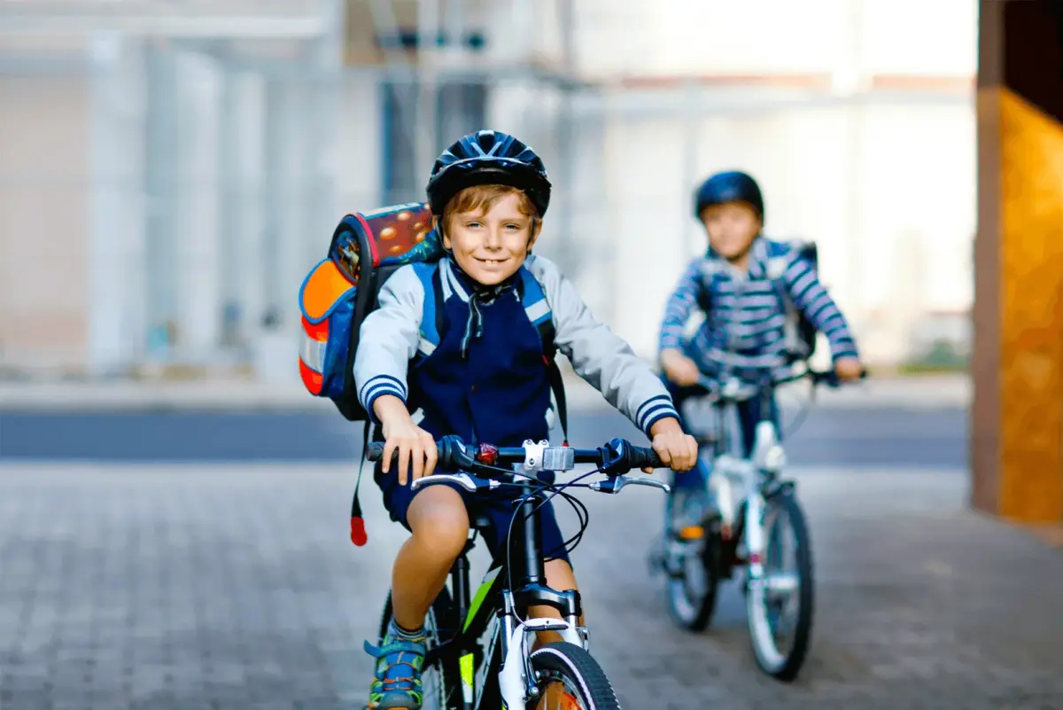 Zwei Kinder radeln mit Helm und Fahrradlicht auf einem sicheren Weg zur Schule.