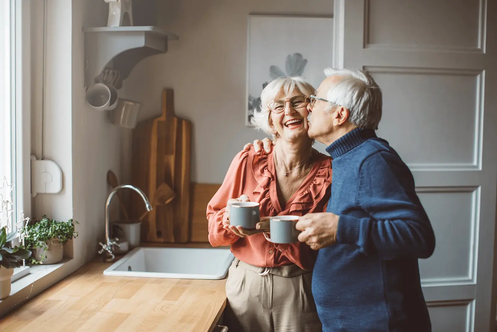 Foto: ein Rentner-Paar steht in der Küche und trinken lachen ihren Kaffee.