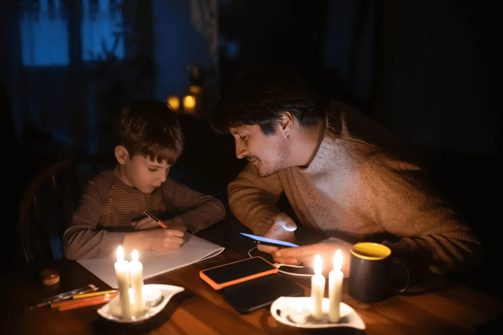Foto: Vater und Sohn sitzen am Tisch mit Kerzen und den Hausaufgaben.