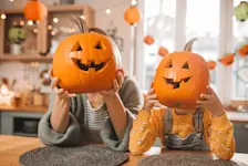 Foto: zwei Kinder halten jeweils einen großen Kürbis vor ihr Gesicht, in das sie ein Gesicht geschnitzt haben.