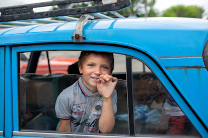 A boy waits in a car while his father purchases hygiene products with a voucher he received from a humanitarian organization.