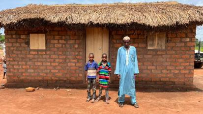 Ibrahim Hassan et sa famille posent devant leur nouvelle maison à Pladama Ouaka - la toute première maison des enfants. Ibrahim a été déplacé au cours des 10 dernières années. © HCR, Francis Donatien Cedric Romane Palike, Préfecture de la Ouaka, République centrafricaine, 2022. 