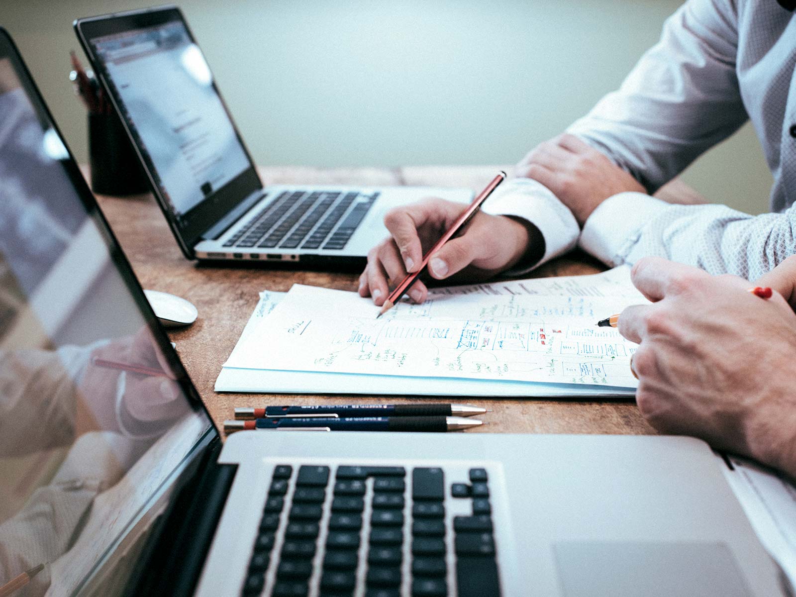 Two people writing on a notepad between two laptops