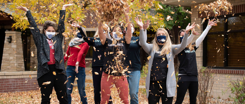 Seven women throw leaves in the air at a volunteer event