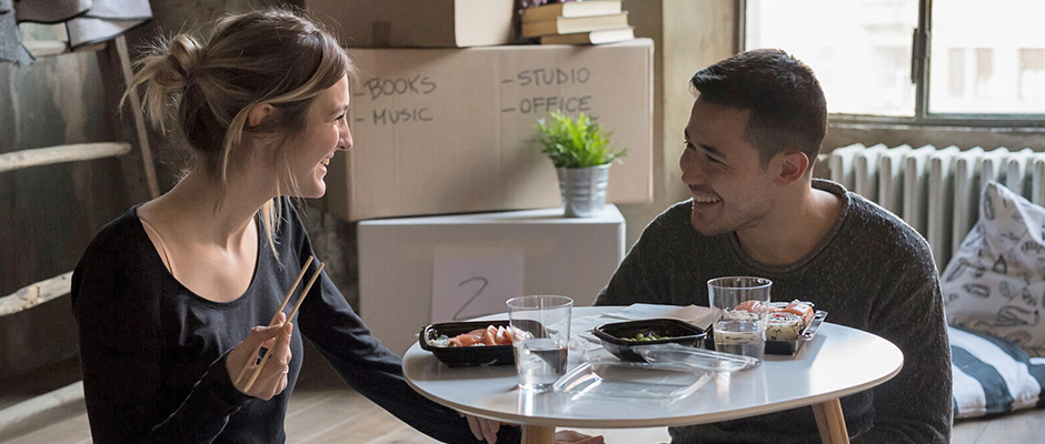 Young couple eating sushi on the floor of their new home with moving boxes in the background