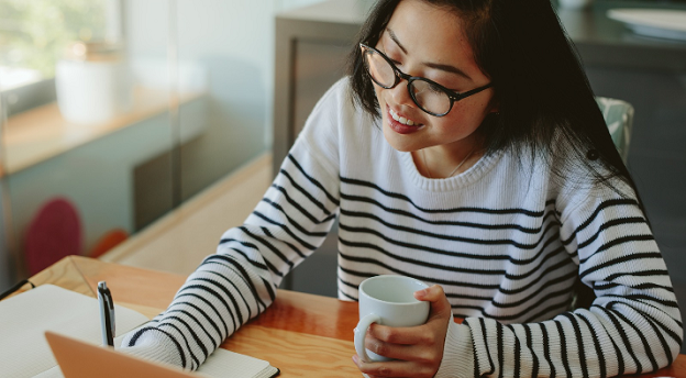 close up image of a female holding a mug and using a laptop