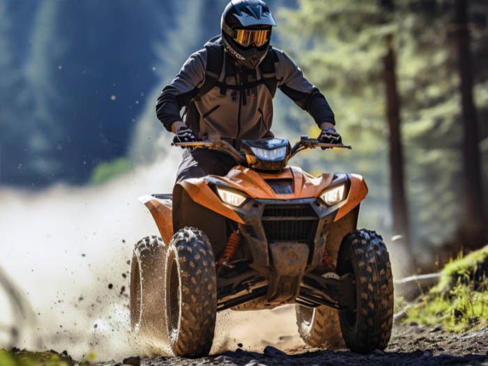 Persona que conduce un quad amarillo con casco levantando una nube de polvo mientras corre por un camino de tierra con montañas y pinos al fondo.