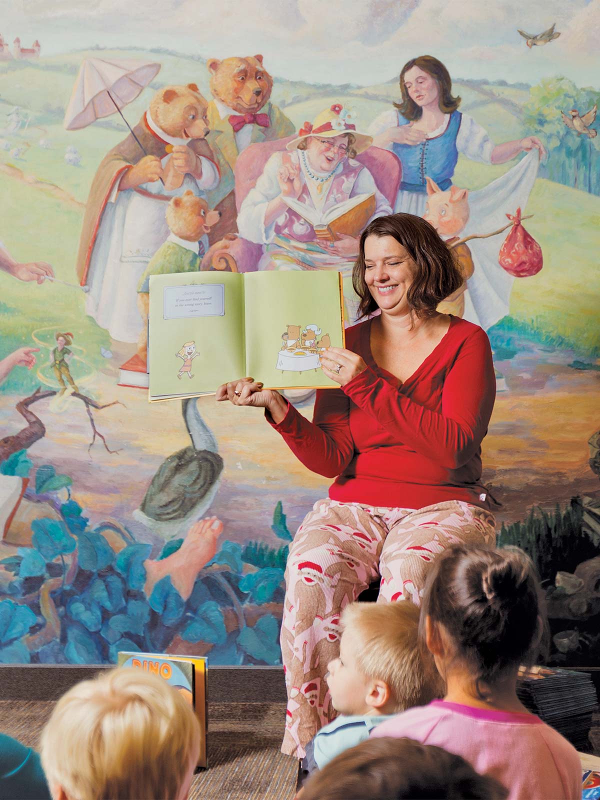 La mujer lee un libro de imágenes en voz alta a una clase de niños de kínder