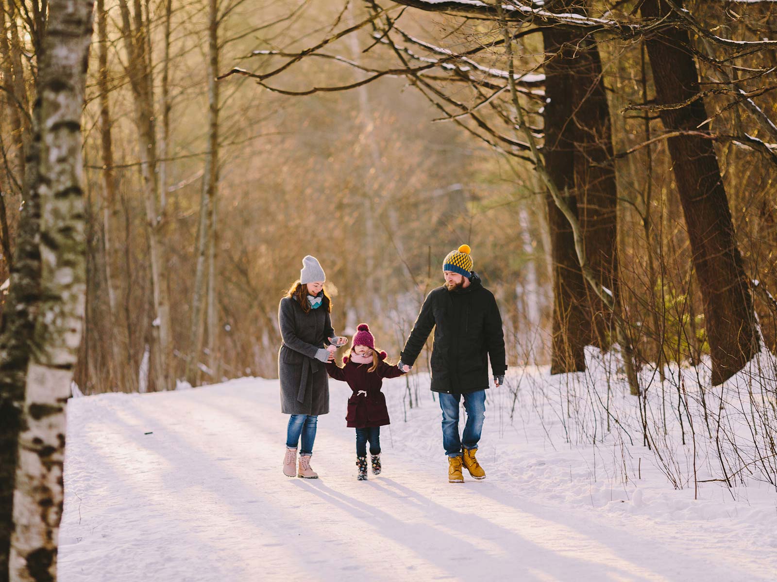 Madre, padre y niña caminando en un bosque de aspen nevado
