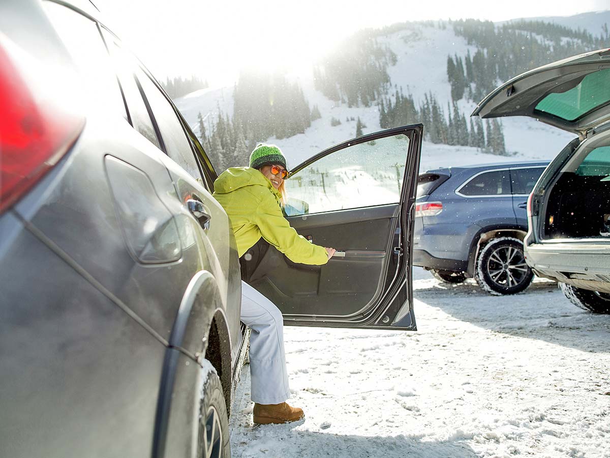 Mujer con equipo de esquí saliendo del vehículo en el aparcamiento de una estación de esquí