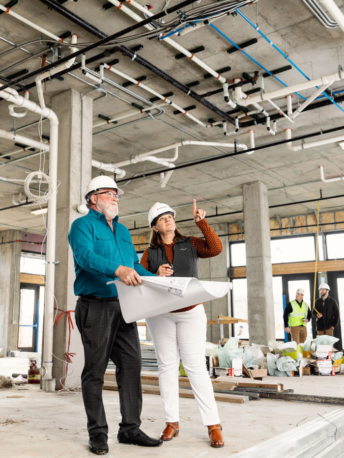 A male and female engineer looking at blueprints while working in commercial space under construction