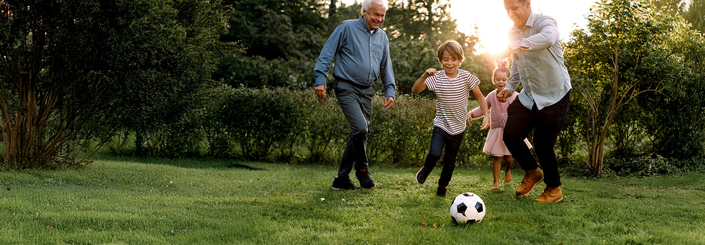 Padre y abuelo jugando al fútbol con niños.