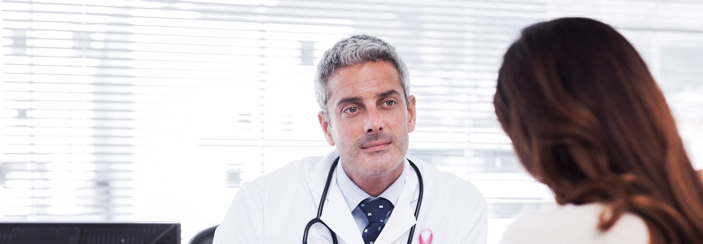 Pink awareness ribbon against the doctor listens to his patient to talk about his illness