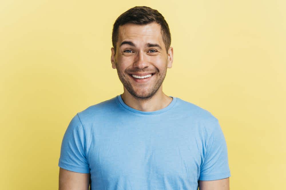 A headshot of a man smiling in front of a yellow background.