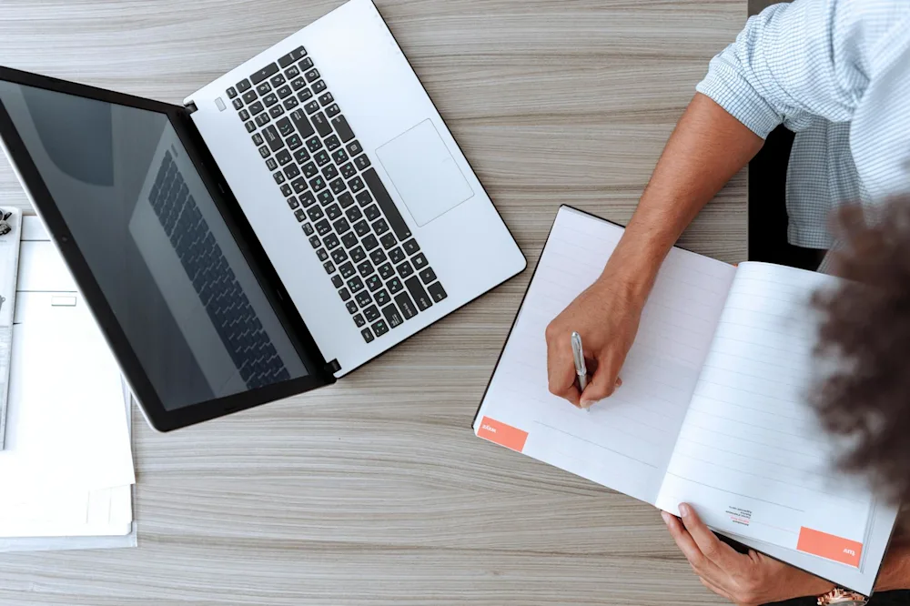UK small business owner reviewing tasks on laptop with notebook
