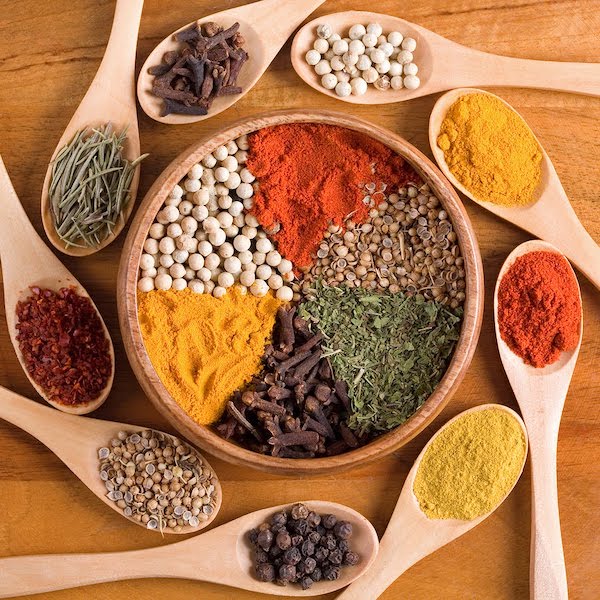 A wooden bowl of colorful spices surrounded by wooden spoons