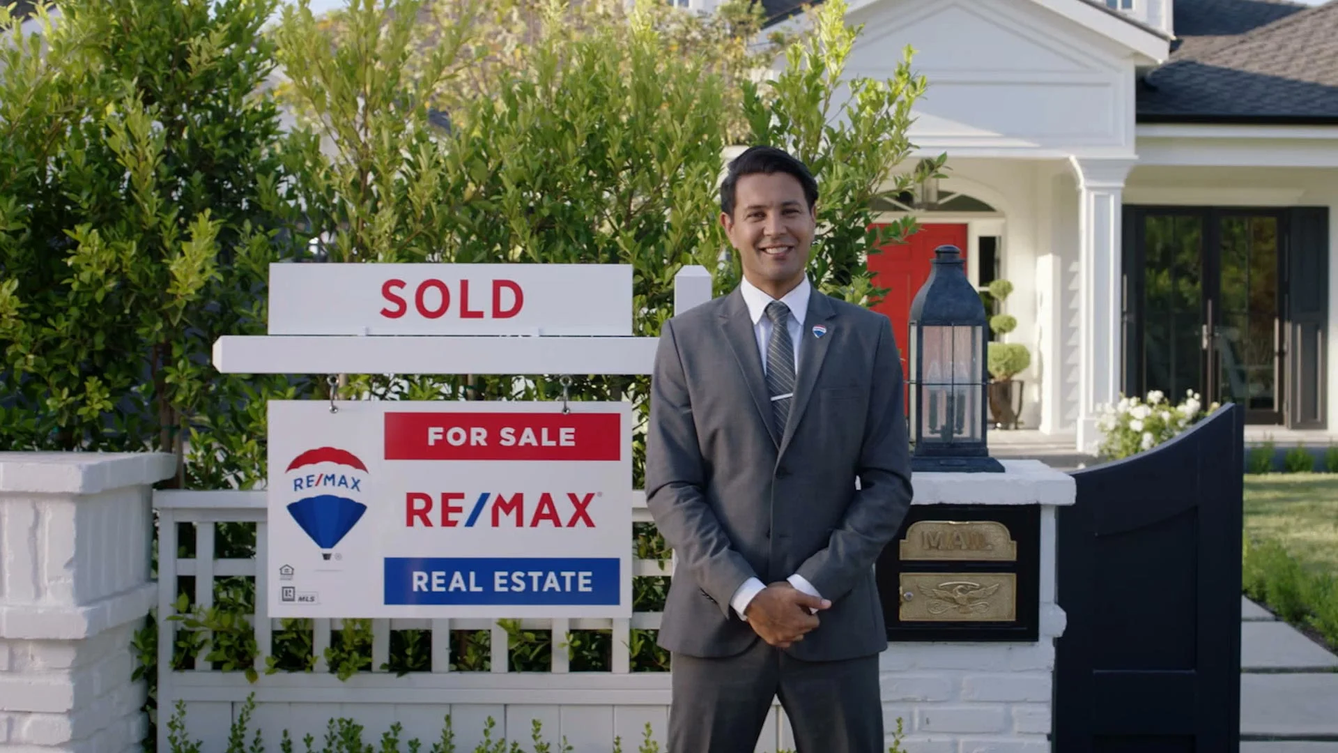A real estate agent standing in front of a house with a RE/MAX "Sold" sign